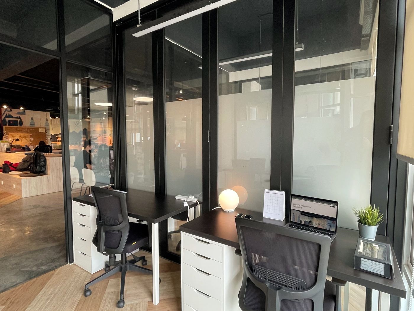 Glass-front private offices at Sandbox Space with the lounge nearby